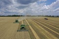 Two harvesters harvest ripe golden wheat in a grain field. Agricultural work in summer. John Deere green yellow combine harvester