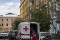 Two health workers in respirators take medication out of an ambulance van with red cross on it