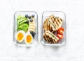 Two healthy office lunch box with sweet, savoury food. Boiled egg, avocado, tuna spinach cheese sandwiches, fruit on a light Royalty Free Stock Photo