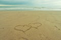 Two hearts drawn in the sand of a beach with a quiet sea and incoming clouds in the back Royalty Free Stock Photo