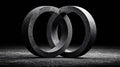 Two heavy dark metallic interlocking rings with a rough texture stand dramatically illuminated against a deep black background Royalty Free Stock Photo