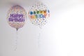 two helium balloons decorated with colored dots and a happy birthday message, with a hanging ribbon, on the roof of a white room, Royalty Free Stock Photo