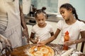 Two helpful girls spreading tomato sauce while cooking pizza