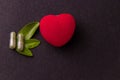 Two herbal capsules with a heart shape on a black blackground and green leaves. Healthy heart concept Royalty Free Stock Photo