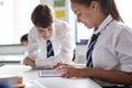 Two High School Students Wearing Uniform Working Together At Desk Using Digital Tablet