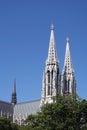 Two high spires on Votivkirche and church roof above green tree branches in the central part of Vienna