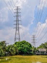 Two high voltage power poles located among the trees along the large ponds and restaurants in city,  High voltage electric poles Royalty Free Stock Photo