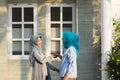 Two hijab women neighbors meet and say hi while smiling and shake hands in front of their house Royalty Free Stock Photo