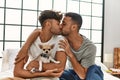 Two hispanic men couple kissing and hugging each other sitting on bed with chihuahua at bedroom Royalty Free Stock Photo