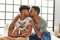 Two hispanic men couple kissing and hugging each other sitting on bed with chihuahua at bedroom Royalty Free Stock Photo