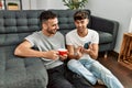 Two hispanic men couple using smartphone and drinking coffee at home Royalty Free Stock Photo