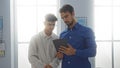 Two hispanic men discuss something on a digital tablet in a bright office, reflecting a modern workplace environment with a focus Royalty Free Stock Photo