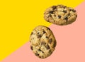 Two homemade chocolate chips cookies flying in air on diagonal duotone pink yellow background. Baking kids birthday party sweets Royalty Free Stock Photo