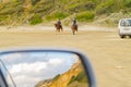 two horses and riders on beach with dunes reflected in car rear vision mirror