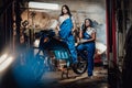 Two brunette women in blue overalls posing next to a sportbike in authentic workshop garage