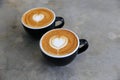 Two hot cups of cappucino on concrete background. Heart shape art latte symbol of love Royalty Free Stock Photo