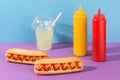 Two hotdogs, a cup of lemonade and squeeze bottles of mustard and ketchup