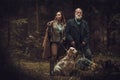 Two hunters with dogs and shotguns in a traditional shooting clothing, posing on a dark forest background. Royalty Free Stock Photo