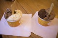 a pair of ice creams in cups on a wooden table ready to eat.
