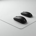 Two identical black wireless computer mice are positioned side by side on a sleek, white mouse pad.
