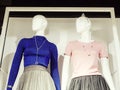 Two identical female mannequins in blue and pink blouses stand turning their heads to the side