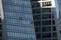 Two industrial alpinists in protection rig-off wadhing vertical glass wall in dense built office cluster