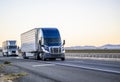 Two industrial bonnet big rigs semi trucks transporting cargo in different semi trailers driving on the straight highway road in Royalty Free Stock Photo