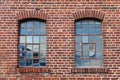 Two industrial looking windows with broken pieces of glas, the window frame is rusted, the brick wall is weathered with many Royalty Free Stock Photo