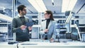 Two Industrial Robotics Engineers Gathered at a Table With Robotic Arm. Female and Male Scientists