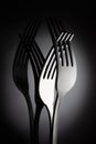 Two interlocking shiny forks on reflective black background for artistic minimalist still life. Shadowy reflection.