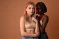 Two international girls in beige bra, african and european girls looking at the camera over dark orange