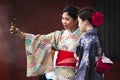 Two Japanese girls taking a selfie with smartphone. Tourists dressed in traditional colorful kimono. Entrance of a shinto temple. Royalty Free Stock Photo