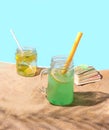 Two jars with cocktail like beverage and paper and reusable silicone straws on the sandy beach, palm leaf shadow, and playing card