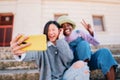 Two joyful cheerful girls taking a selfie while sitting together outdoors and showing peace gesture Royalty Free Stock Photo