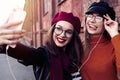 Two joyful cheerful girls taking a selfie while walking in the city street having fun. Royalty Free Stock Photo