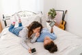 Two joyful girls talking and holding mobile phones while lying in bed together Royalty Free Stock Photo