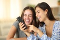 Two joyful roommates laughing watching media on phone