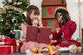 Two joyful young Asian girls are enjoying reading a Christmas fairy tale story in a book together Royalty Free Stock Photo