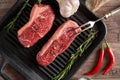 Two juicy, fresh new york steaks in a grill pan with sprigs of rosemary, a head of garlic, pods of red chili pepper, a meat fork Royalty Free Stock Photo