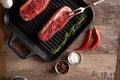Two juicy, fresh new york steaks in a grill pan with sprigs of rosemary, a head of garlic, pods of red chili pepper, a meat fork Royalty Free Stock Photo