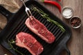 Two juicy, fresh new york steaks in a grill pan with sprigs of rosemary, a head of garlic, pods of red chili pepper, a meat fork Royalty Free Stock Photo