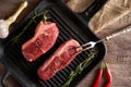 Two juicy, fresh new york steaks in a grill pan with sprigs of rosemary, a head of garlic, pods of red chili pepper, a meat fork Royalty Free Stock Photo