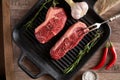 Two juicy, fresh new york steaks in a grill pan with sprigs of rosemary, a head of garlic, pods of red chili pepper, a meat fork Royalty Free Stock Photo