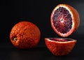 Two juicy ripe citruses - Sicilian red orange cut in half, located on a stone black background. Close-up Royalty Free Stock Photo