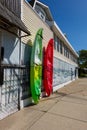 Two kayaks, one red and the other green and yellow, chained standing up next to the wall of a building