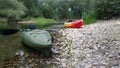 Two kayaks on the side of a river. There are trees around and rocks on the shore.