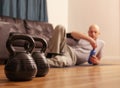 Two kettle bells in focus. Bald man laying on the floor of living room with a blue bottle of water in his hand out of focus, Royalty Free Stock Photo
