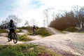 two kids on bicycles ride on a dirt jump track in bright sun under a blue sky.