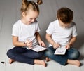 Two kids boy and girl in white t-shirts and blue jeans sit close to each other and play battleship Royalty Free Stock Photo