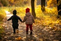 Two kids, boy and girl of two years old, walk hand in hand along path on warm autumn day in park Royalty Free Stock Photo